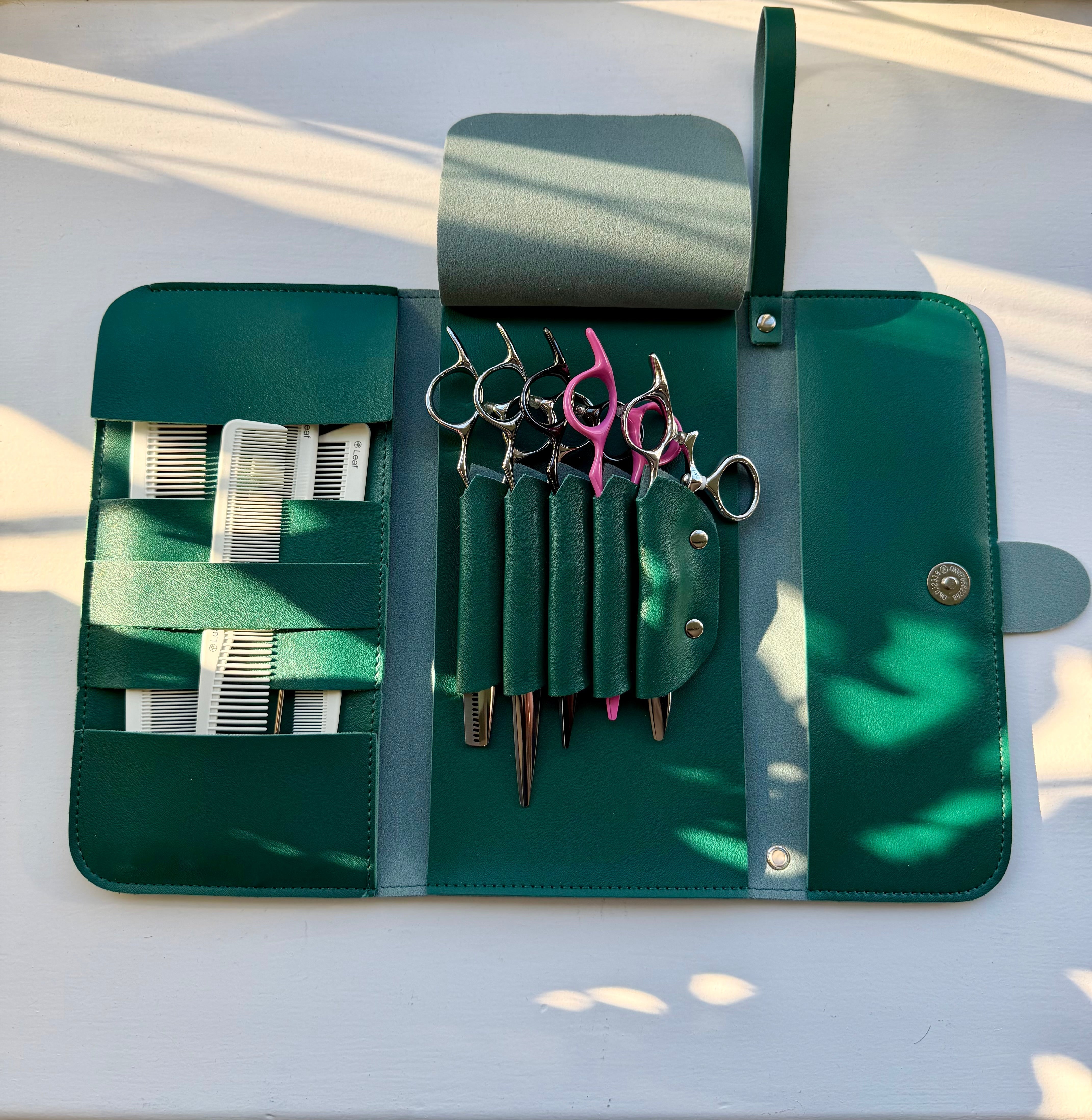 Open forest green Kit Roll by Leaf holding scissors and combs