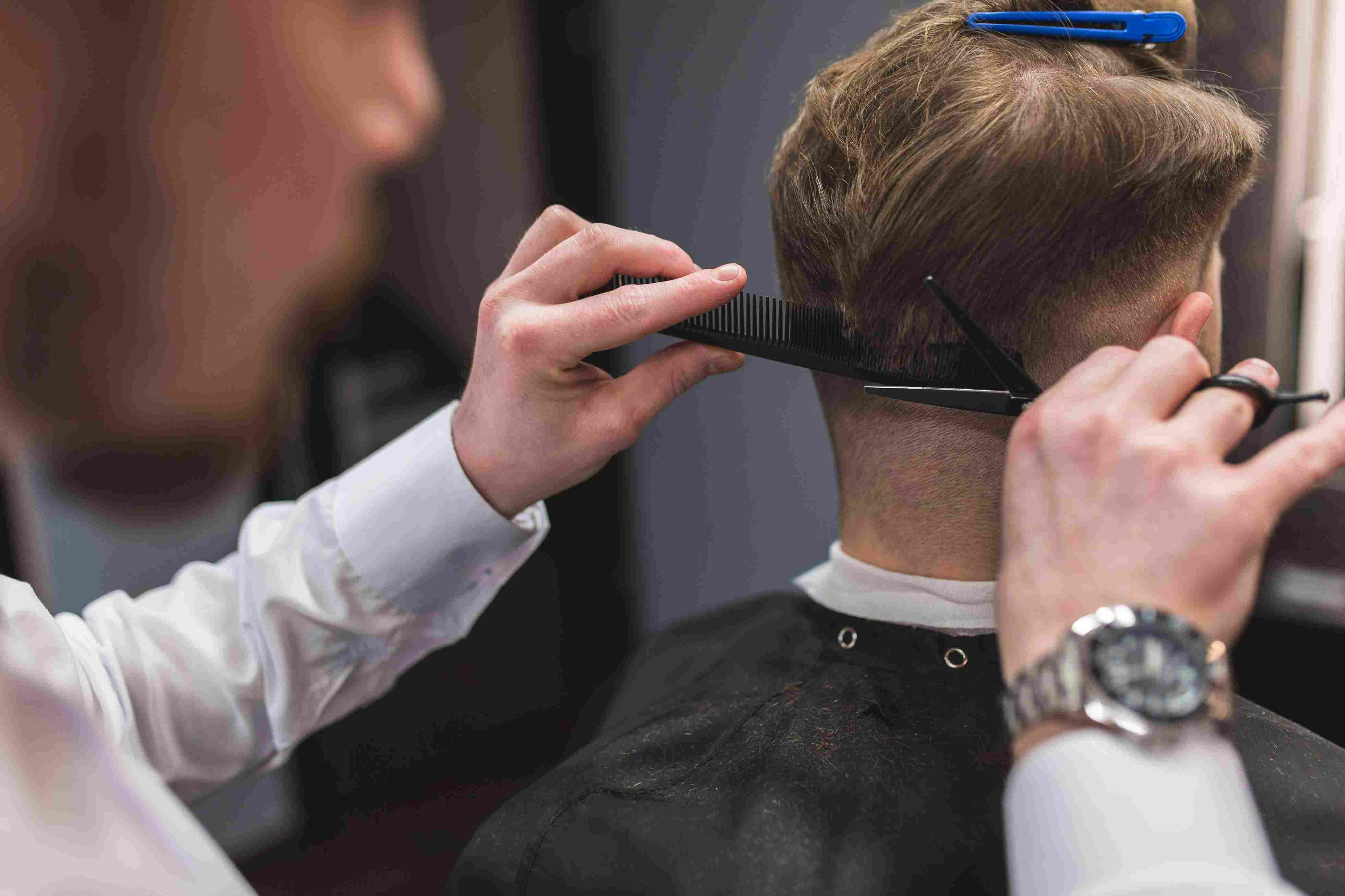 hairdresser cutting man's hair with hairdressing scissors